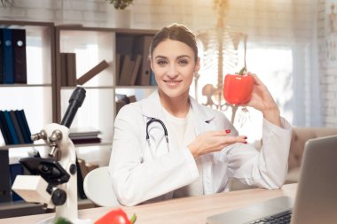 Kadın doktor stetoskop ile mikroskop ofis masasında oturuyor. Kadın kırmızı biber tutuyor.