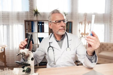 Doktor stetoskop ile mikroskop ofis masasında oturuyor. Adam kabı tutuyor.