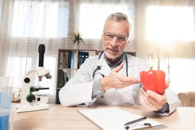 Doktor stetoskop ile mikroskop ofis masasında oturuyor. Adam kırmızı biber tutuyor.
