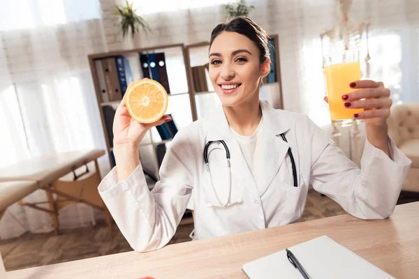 Kadın doktor stetoskop ile mikroskop ofis masasında oturuyor. Kadın portakal ve meyve suyu tutuyor.