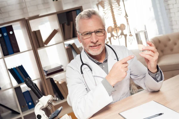 Doktor stetoskop ile mikroskop ofis masasında oturuyor. Adam su tutuyor. — Stok fotoğraf