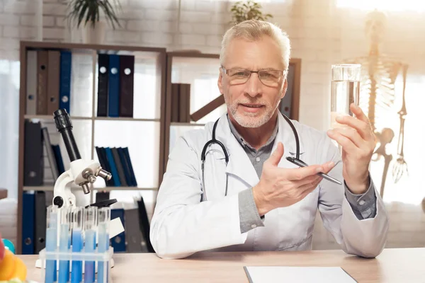 Doktor stetoskop ile mikroskop ofis masasında oturuyor. Adam su tutuyor. — Stok fotoğraf