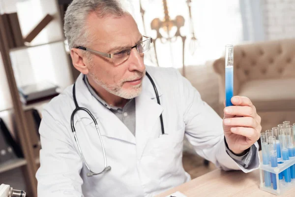 Doktor mikroskop ve stetoskopla ofiste masada oturuyor. Adam elinde ilaç bardağı tutuyor.. — Stok fotoğraf