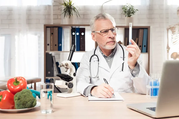 Doktor stetoskop ile mikroskop ofis masasında oturuyor. Adam kabı tutuyor. — Stok fotoğraf