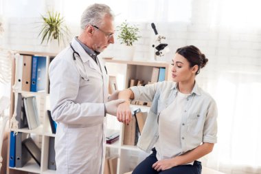Doktor stetoskop ve erkek hasta Office ile. Doktor kadının kolunu incelenmesi.
