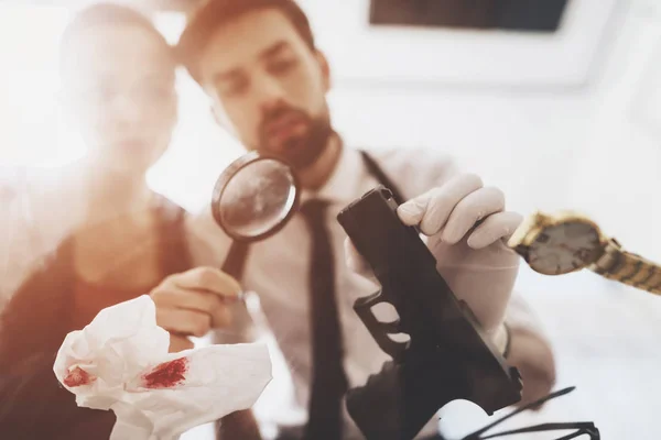 Private detective agency. Man and woman are looking at gun with magnifying glass. — Stock Photo, Image