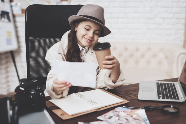 Prive-detective bureau. Meisje zit bij bureau kijken naar verschillende foto's en koffie drinken. — Stockfoto