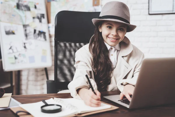 Agencja prywatnego detektywa. Mała dziewczynka siedzi przy biurku notatek w pobliżu laptopa. — Zdjęcie stockowe