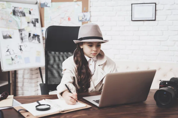 Agencja prywatnego detektywa. Mała dziewczynka siedzi przy biurku notatek w pobliżu laptopa. — Zdjęcie stockowe