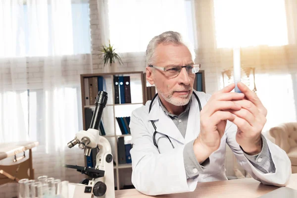 Doktor stetoskop ile mikroskop ofis masasında oturuyor. Adam kabı tutuyor. — Stok fotoğraf