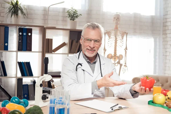 医師は顕微鏡と聴診器のオフィスで机に座って。男は、赤唐辛子を保持しています。. — ストック写真