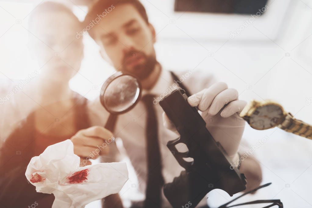 Private detective agency. Man and woman are looking at gun with magnifying glass.