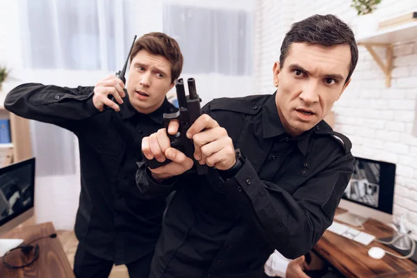 Two men of guards hold a gun and walkie-talkie.