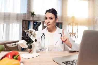 Kadın doktor stetoskop ile mikroskop ofis masasında oturuyor. Kadın mikroskobu arıyor.