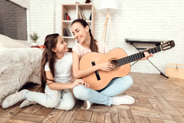 Mamá y su hija están sentadas en el suelo en casa tocando la guitarra. Cantan a la guitarra . — Foto de Stock