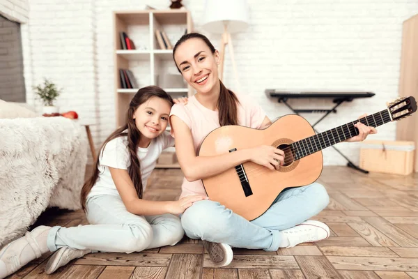 Mamá y su hija están sentadas en el suelo en casa tocando la guitarra. Cantan a la guitarra . — Foto de Stock