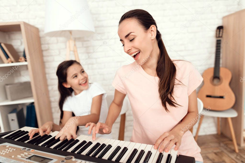Mom and girl are playing the synthesizer at home. They rest and have fun.