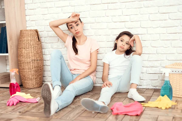 女子和女儿在累人房子后休息。他们背靠着墙坐在地板上休息 — 图库照片