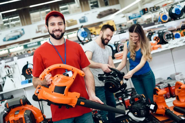 Salesman is posing with new leaf blower with couple of clients in background in power tools store. — Stock Photo, Image