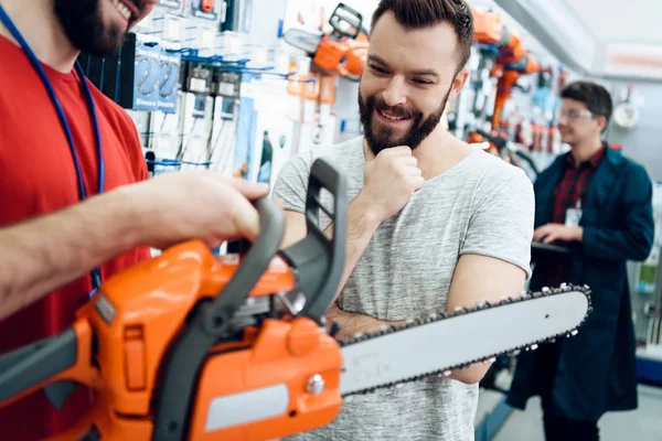 Продавец показывает бородатому клиенту новую бензопилу в магазине электроинструментов . — стоковое фото