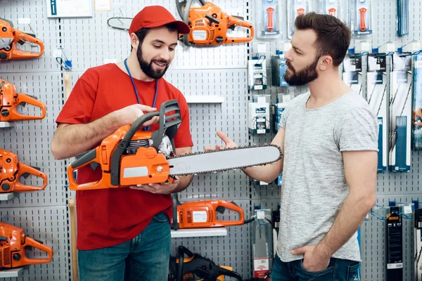 Säljare är visar skäggiga klienten nya motorsåg i power tools butik. — Stockfoto