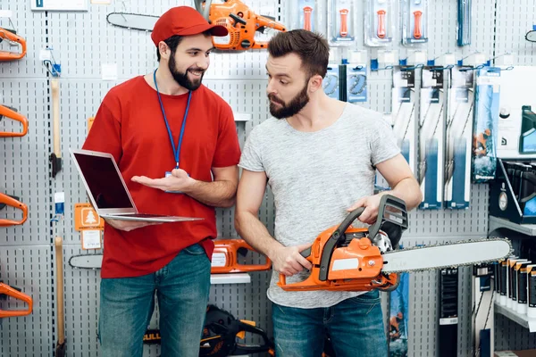 Salesman показує бородатий клієнт нова бензопила, пояснюючи подробиці на ноутбуці в магазині електроінструментів . — стокове фото