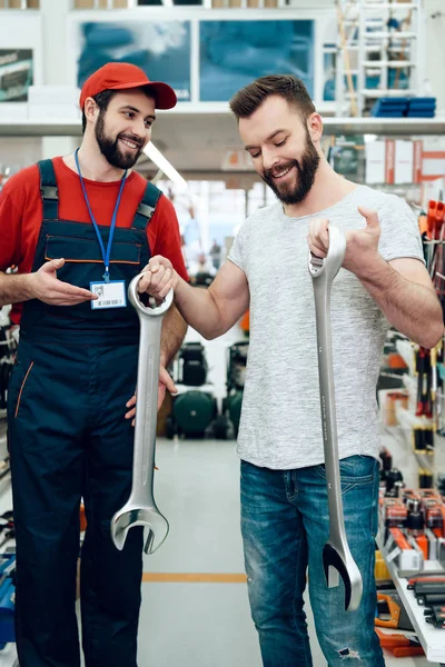 Vendedor e cliente barbudo posando com chaves gigantes na loja de ferramentas elétricas . — Fotografia de Stock