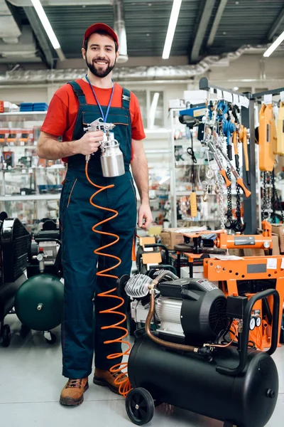 Vendedor está posando com compressor pulverizador de tinta em primeiro plano na loja de ferramentas elétricas . — Fotografia de Stock