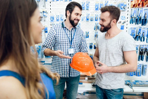 Vendedor está mostrando casal de clientes novo capacete de construção na loja de ferramentas elétricas . — Fotografia de Stock