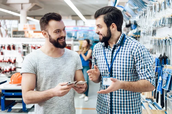 Verkoper vertoont bebaarde cli├½nt-selectie van apparatuur in power tools winkel. — Stockfoto