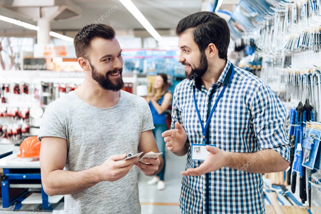 Salesman is showing bearded client selection of equipment in power tools store.