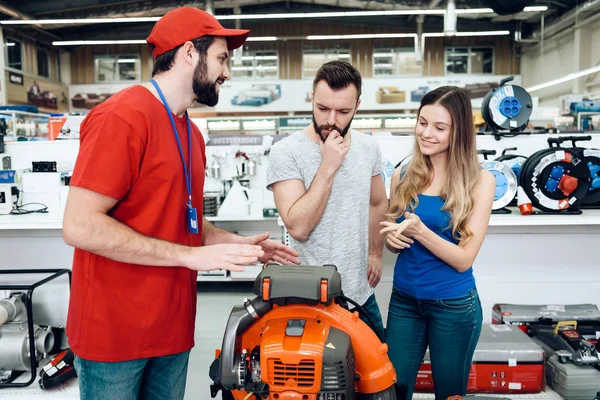 Venditore sta spiegando i dettagli circa il ventilatore del foglio alla coppia dei clienti nel deposito degli attrezzi elettrici . — Foto Stock