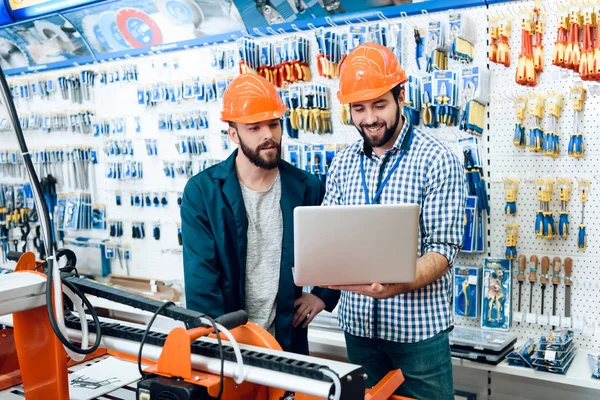 Dois vendedores estão discutindo a seleção de equipamentos perto da máquina de trabalhar madeira na loja de ferramentas elétricas . — Fotografia de Stock