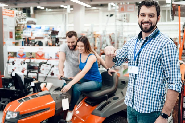 Salesman is posing with couple of clients and keys for cleaning machine in power tools store. — Stock Photo, Image