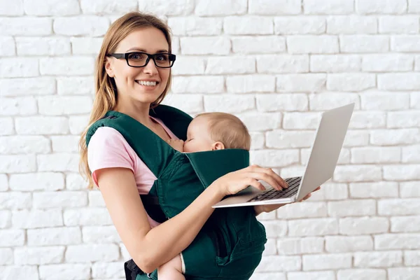 Mom with laptop holding newborn in baby sling. — Stock Photo, Image