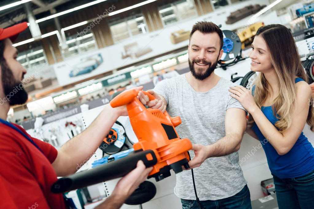 Salesman is giving new leaf blower to couple of clients in power tools store.