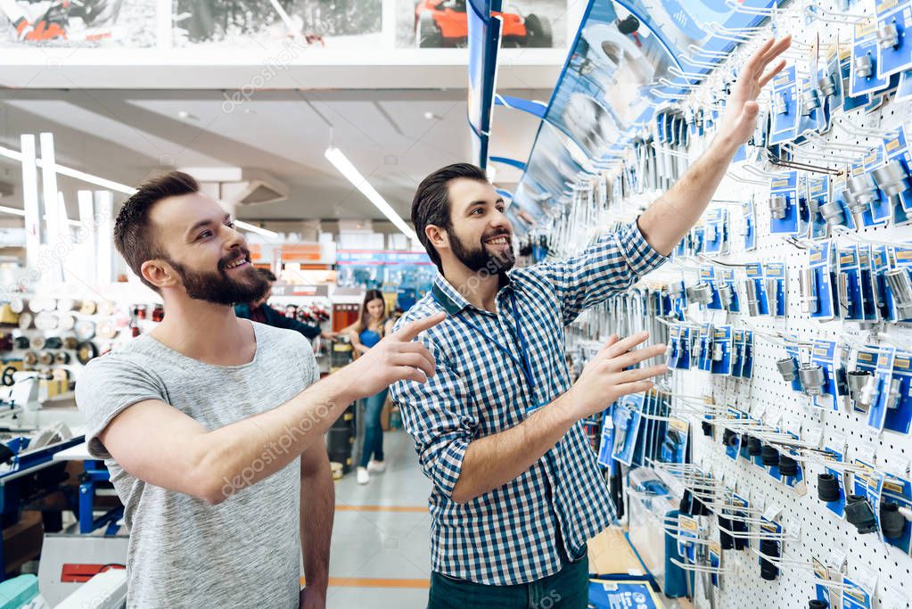 Salesman is showing bearded client selection of equipment in power tools store.