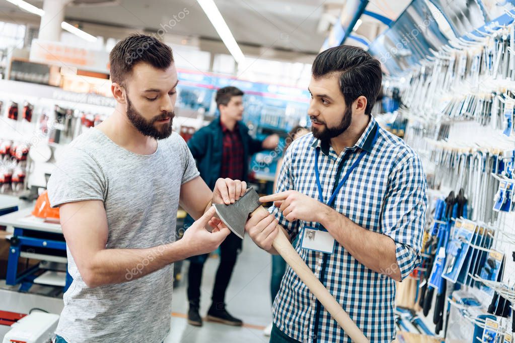 Salesman is showing bearded client new axe in power tools store.