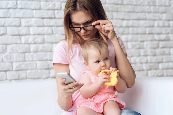 Jovem mãe com pequeno bebê usando smartphone . — Fotografia de Stock