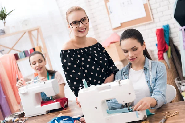 Three women at garment factory. They are sitting behind sewing machines. — Stock Photo, Image