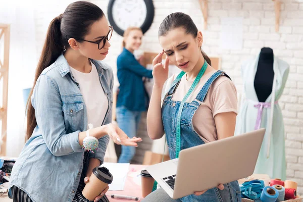 Três raparigas na fábrica de roupas. Eles estão à procura de desing para novo vestido no laptop . — Fotografia de Stock