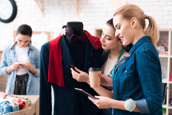 Three girls at garment factory with new suit. One of them is holding scissors.