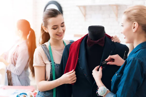 Tres chicas en la fábrica de ropa con traje nuevo. Uno de ellos sostiene tijeras . —  Fotos de Stock