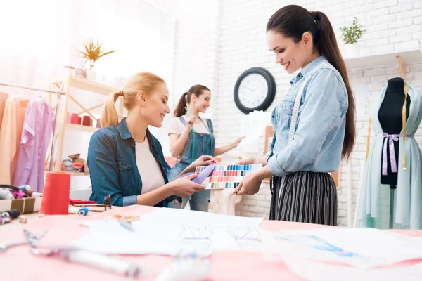 Drie meisjes in kledingstuk fabriek. Ze kijken naar kleuren voor nieuwe jurk op patroon. — Stockfoto