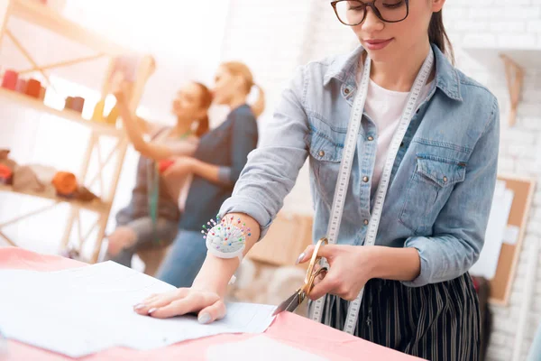 Three girls at garment factory. One of them is making cut-out for new dress. — Stock Photo, Image