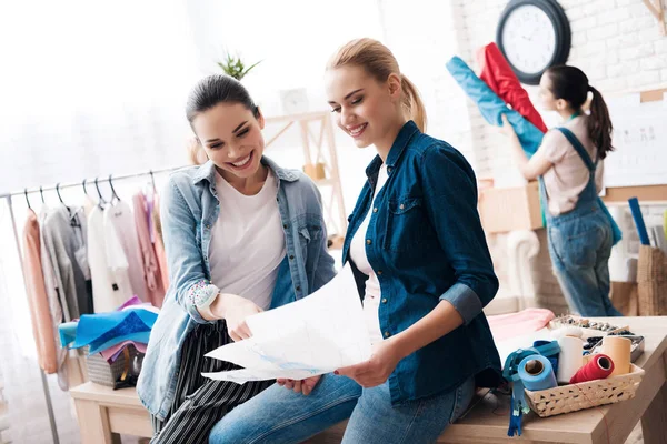 Three girls at garment factory. Two of them are looking at new designs and smiling. — Stock Photo, Image