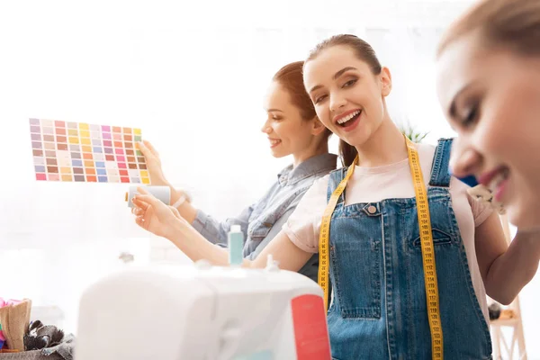 Three girls at garment factory. They are choosing colors for new dress. — Stock Photo, Image