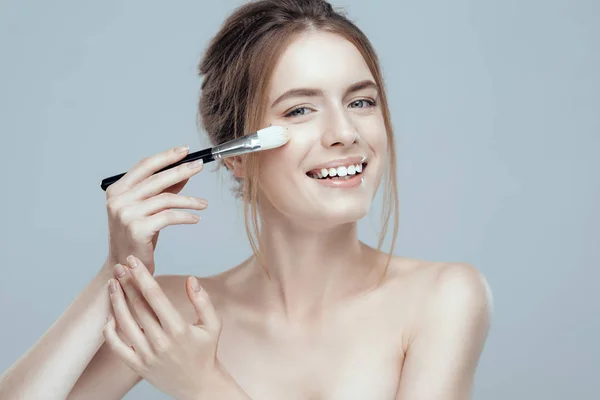 Foto de cerca de una hermosa chica con un cepillo de maquillaje. Ella tiene la piel limpia y uniforme, cabello rubio . —  Fotos de Stock