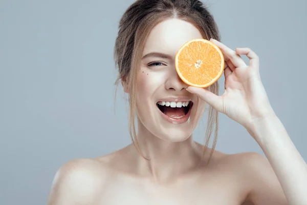 Красива жінка обличчям з соковитим апельсином на сірому фоні. Природна краса і спа . — стокове фото
