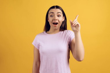 Hevesli genç kız ile işaret parmağı kadar duruyor. Bir fikrim var. Düşünce kavramı nesil. Sarı arka plan üzerinde izole.